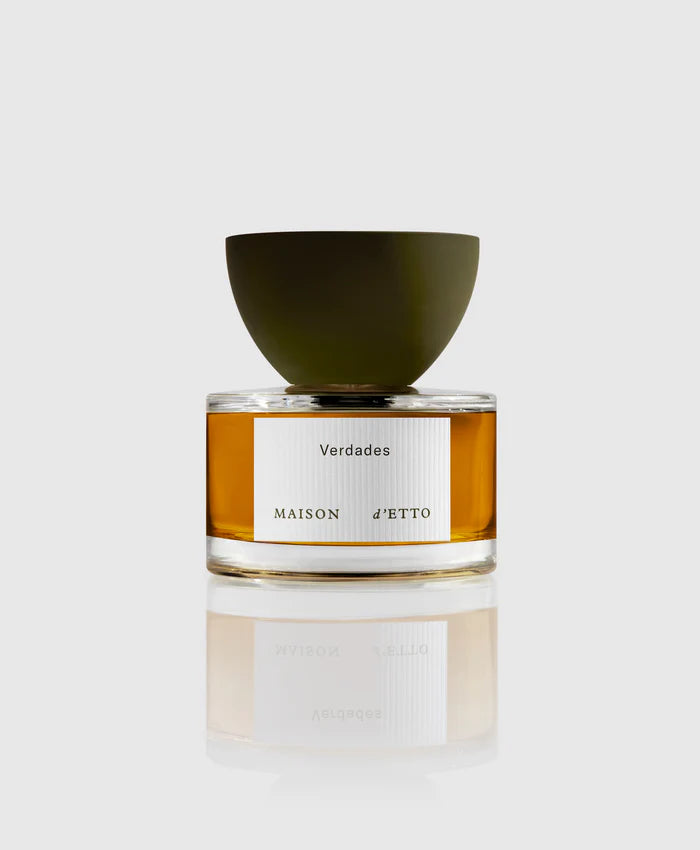 A bottle of 'Verdades Eau de Parfum' by Maison d'Etto with a clear glass and a green cap, displaying the yellow-colored perfume.