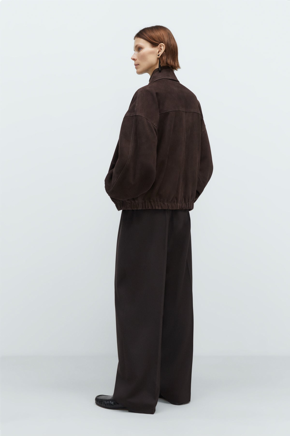 Person wearing a brown jacket and black pants on a white background