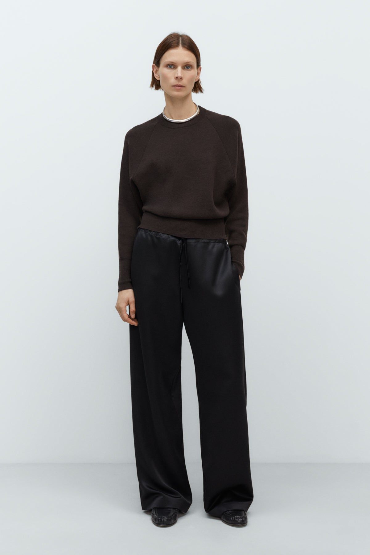 Person wearing a dark cashmere sweater and black pants on a white background