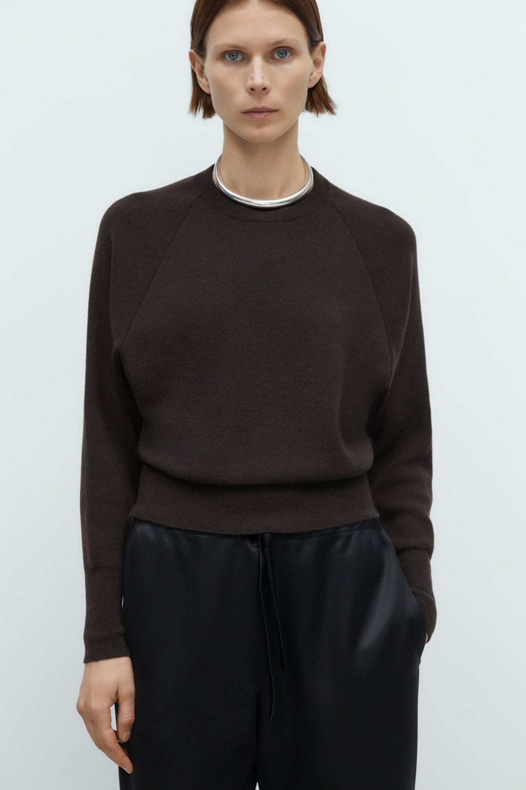 Person wearing a dark brown sweater and black pants on a white background