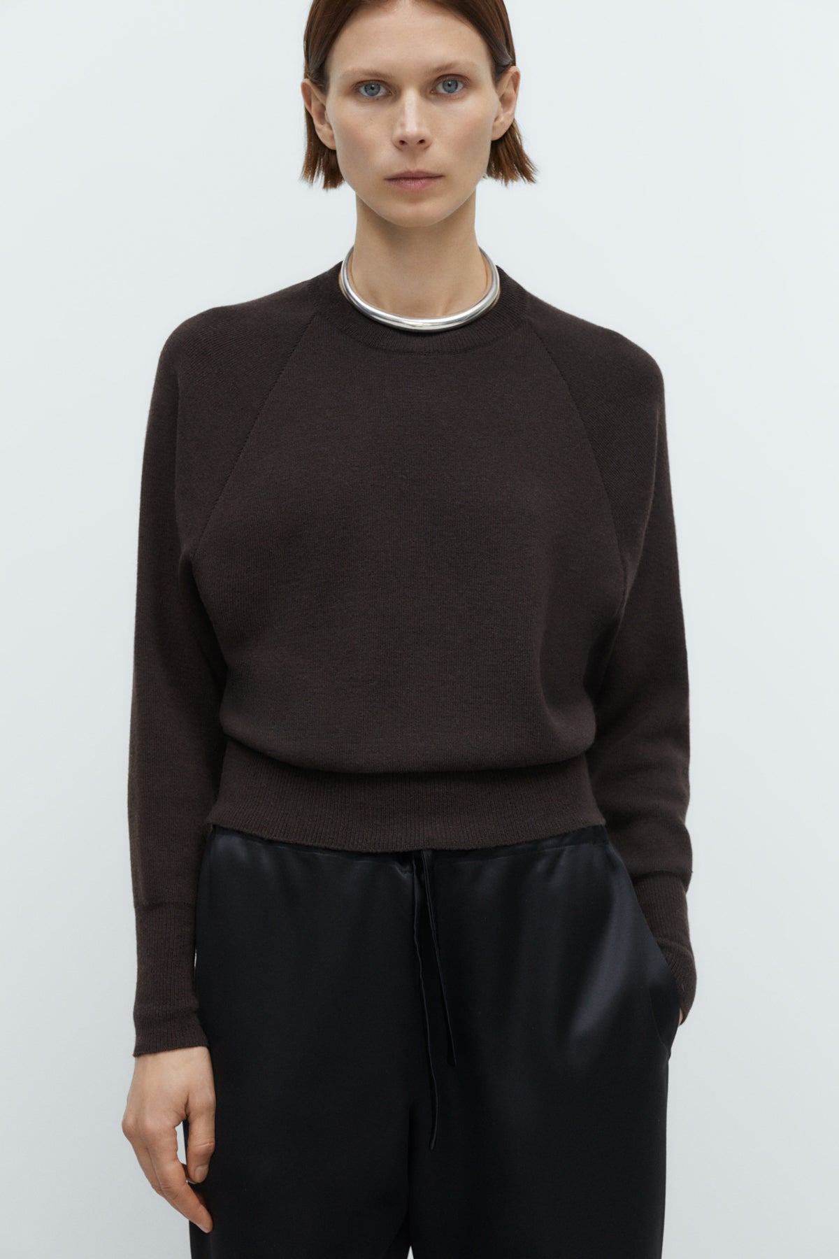 Person wearing a dark brown sweater and black pants on a white background