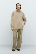 Person wearing a beige sweater and pants against a white background