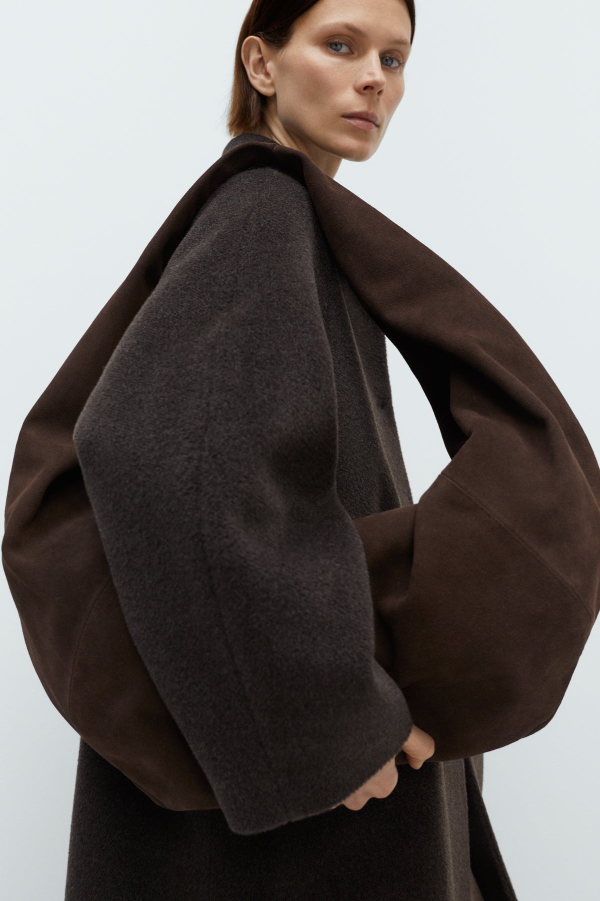 Person carrying oversized crossbody brown bag against a white background.