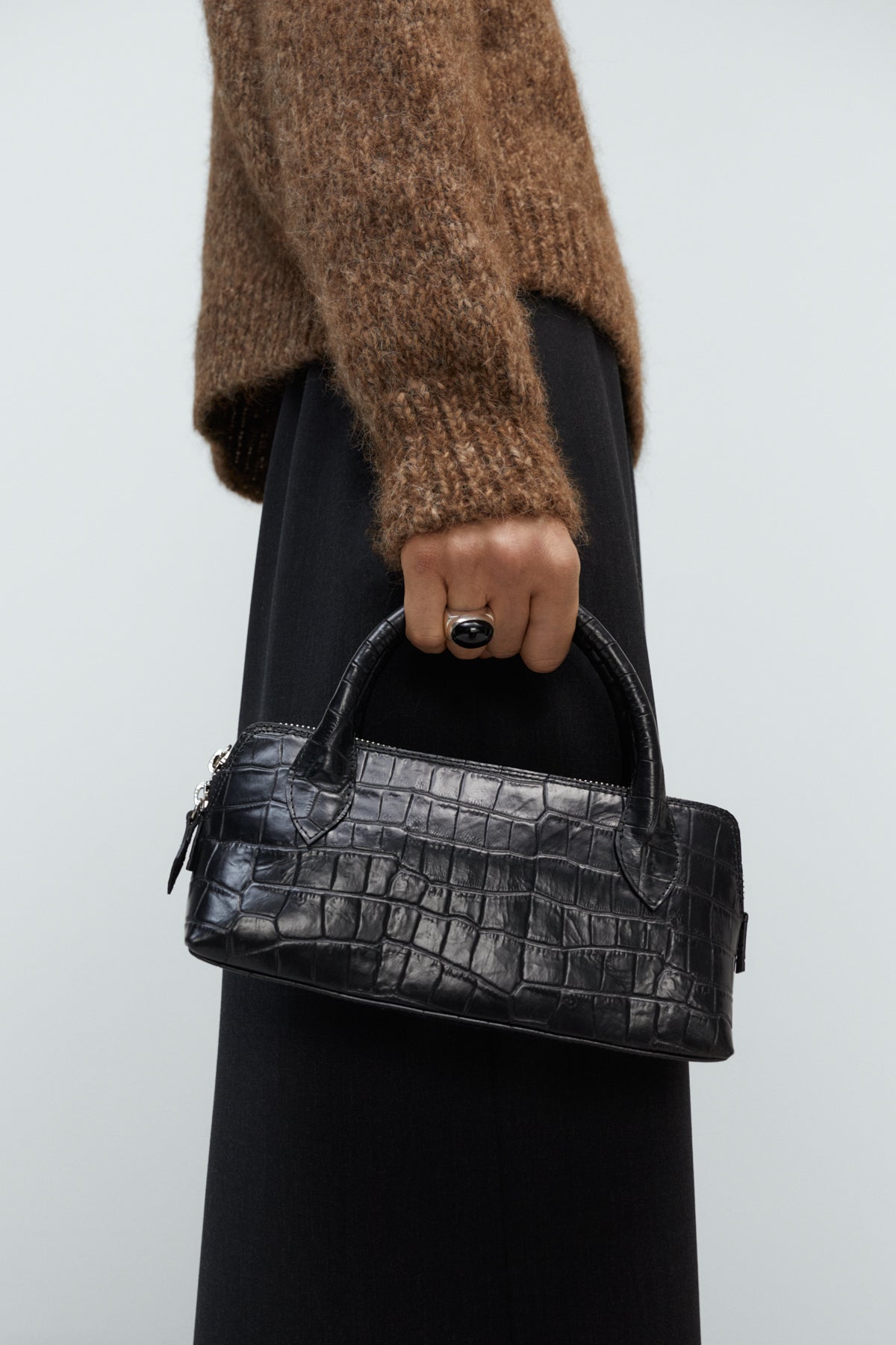 Person holding a black crocodile-patterned handbag against a plain background