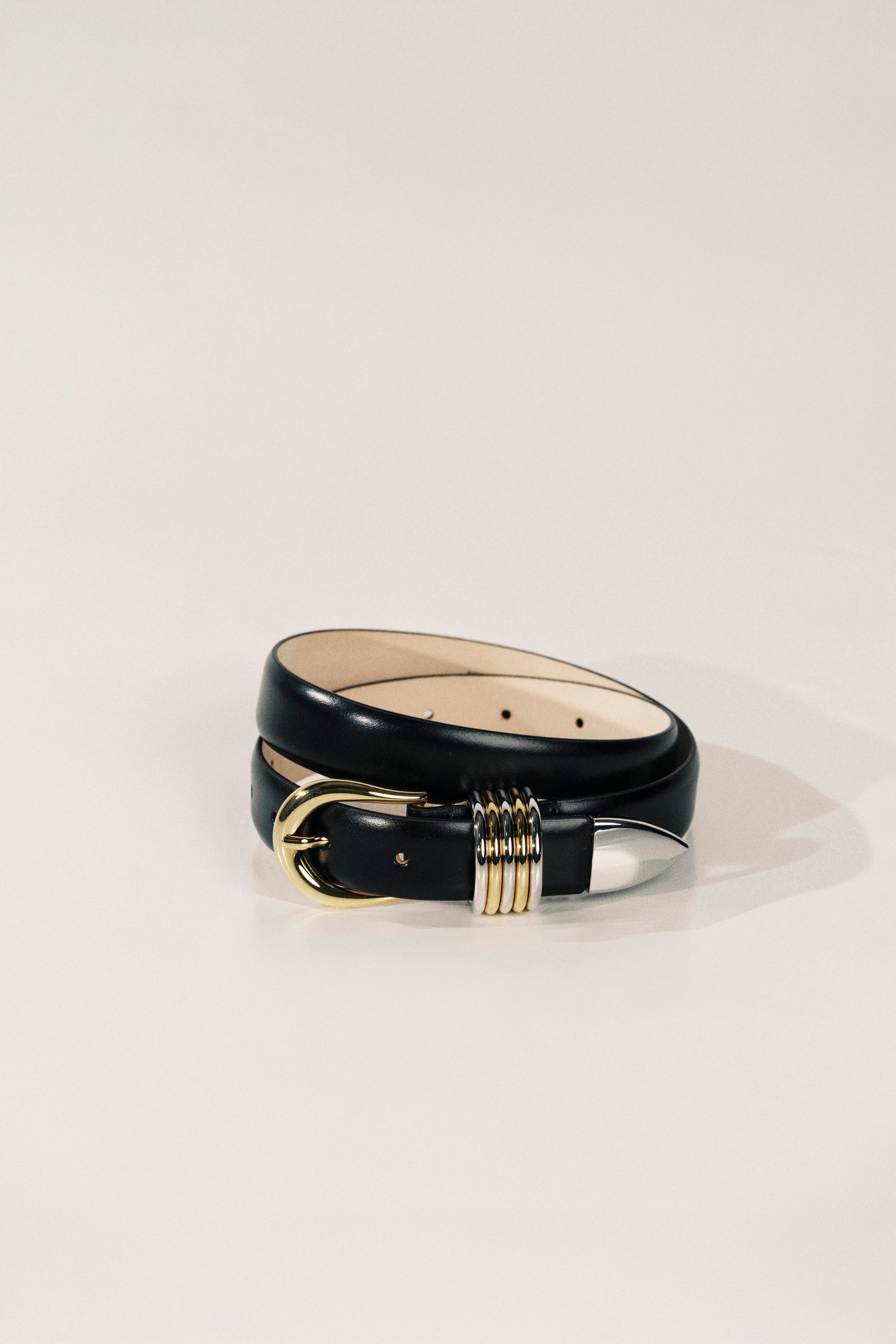 Black leather belt with gold buckle on a light beige background