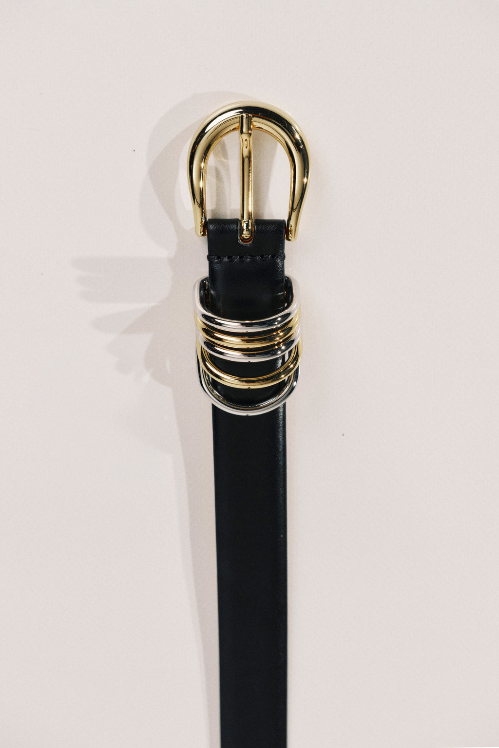 Black belt with a gold buckle on a light pink background