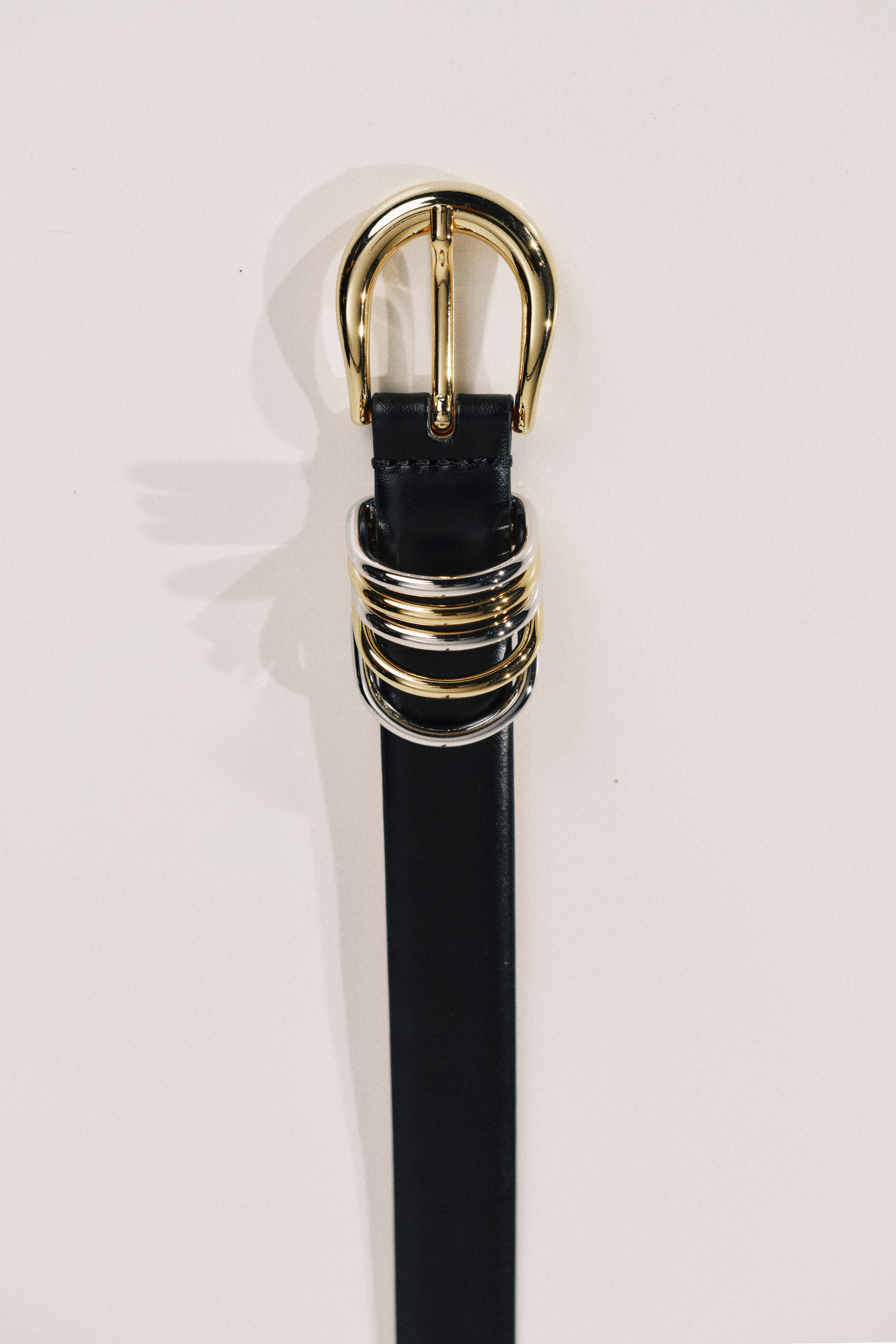 Black belt with a gold buckle on a light pink background