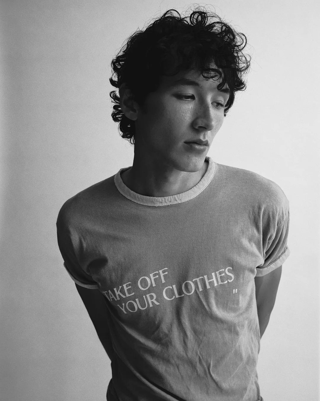 Person wearing a t-shirt with text 'TAKE OFF YOUR CLOTHES' on a plain background