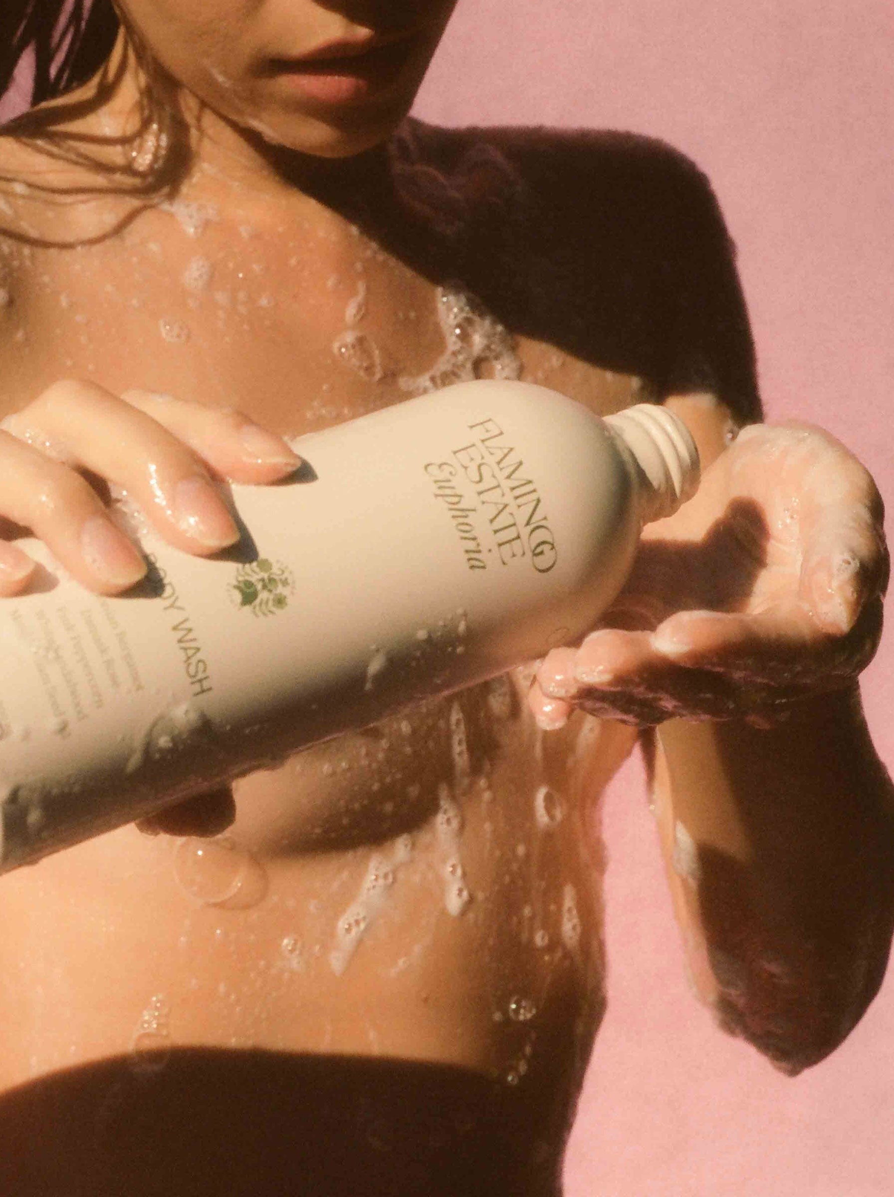 Person using a bottle of body wash against a pink background