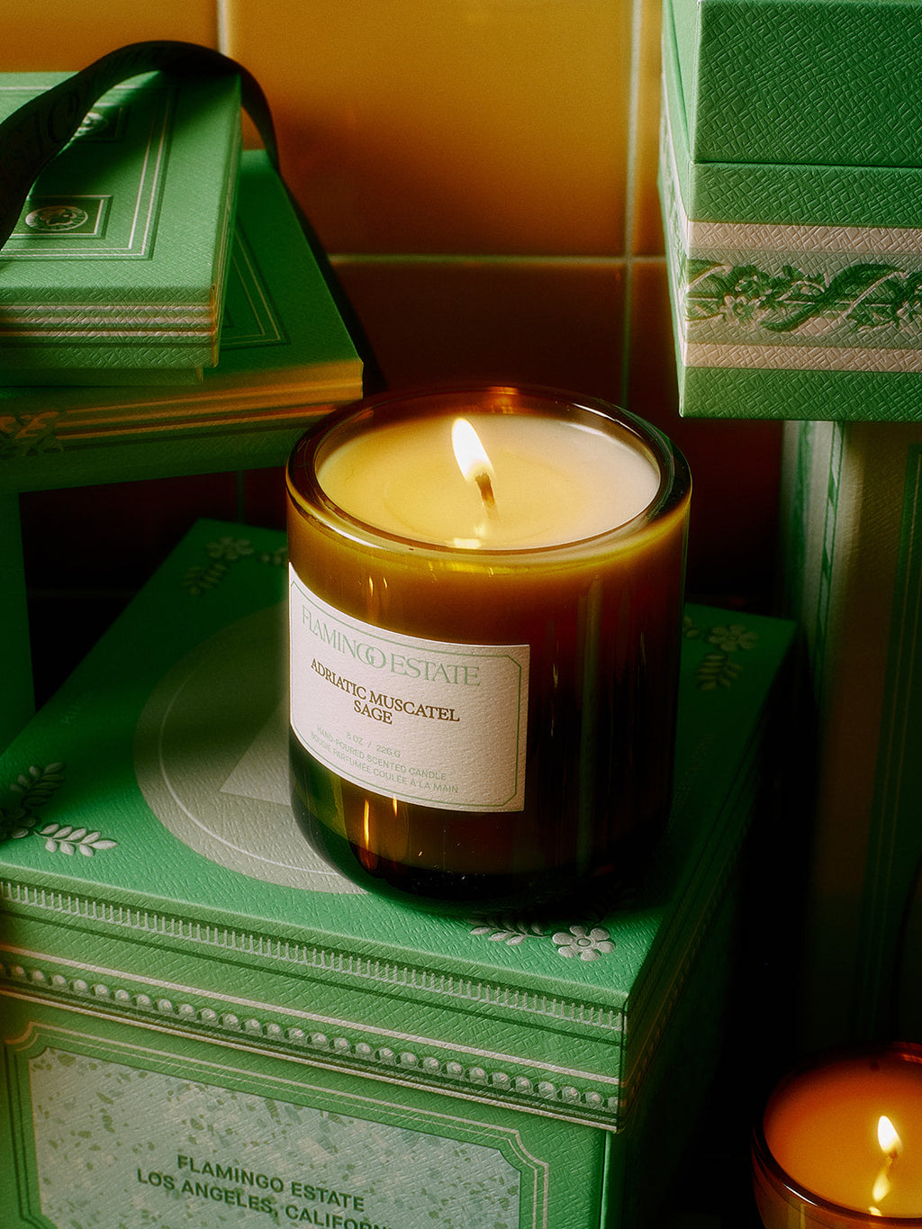 Candle in a glass jar with a label on green decorative boxes.