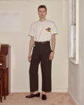 Person wearing a white t-shirt with a colorful pocket design and dark pants in a room.