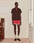 Person wearing a brown shirt and red shorts standing in a room with a piano.