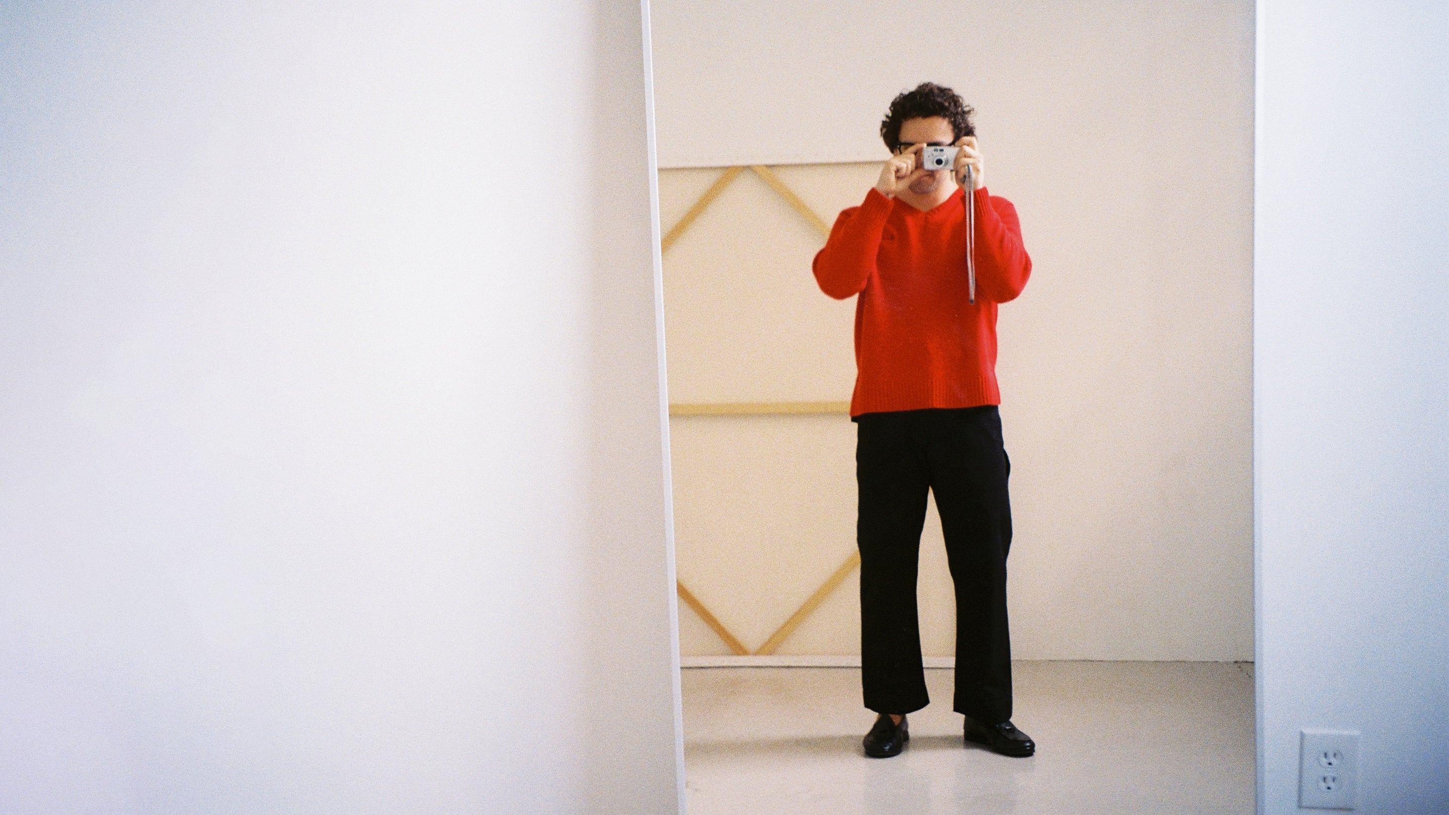 Person taking a photo of themselves in a mirror wearing a red sweater and black pants.