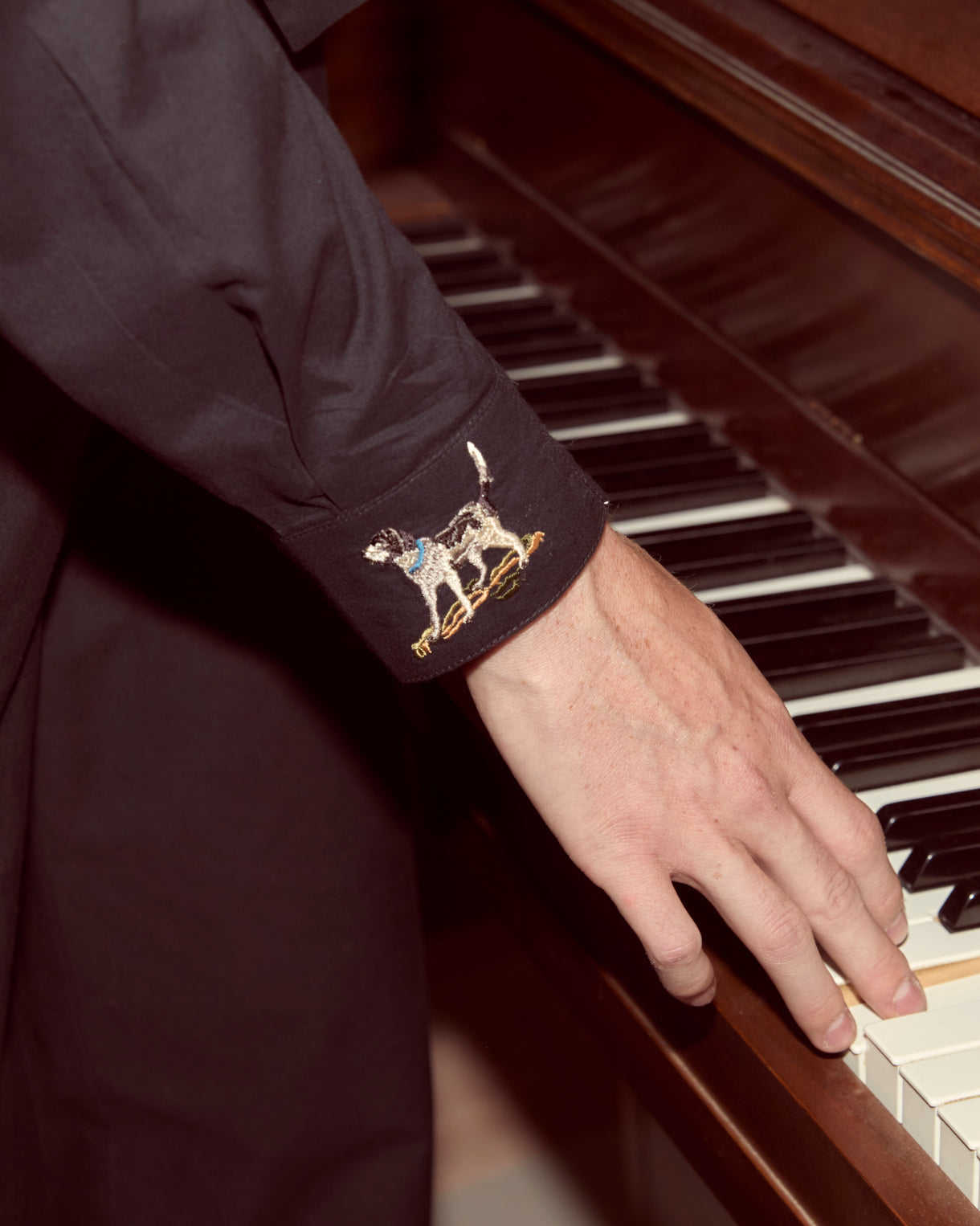 Person playing a piano with a close-up of their hand on the keys, wearing a dark shirt with a decorative cuff.