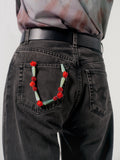 Person wearing black jeans with a decorative floral wristlet on the back pocket against a plain background