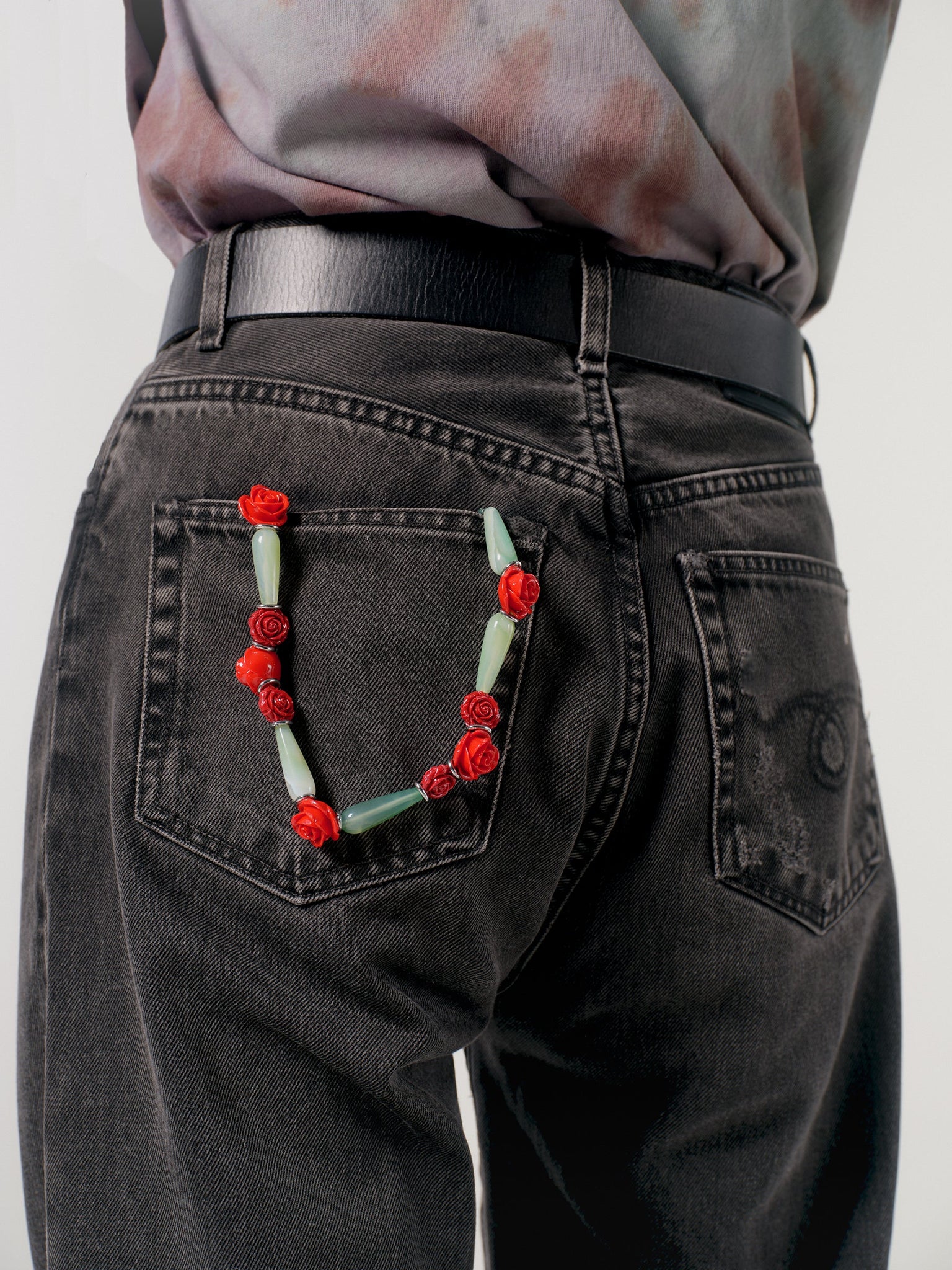 Person wearing black jeans with a decorative floral wristlet on the back pocket against a plain background