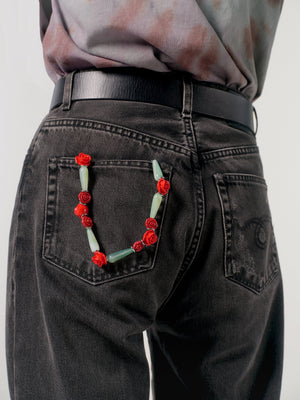 Person wearing black jeans with a decorative floral wristlet on the back pocket against a plain background