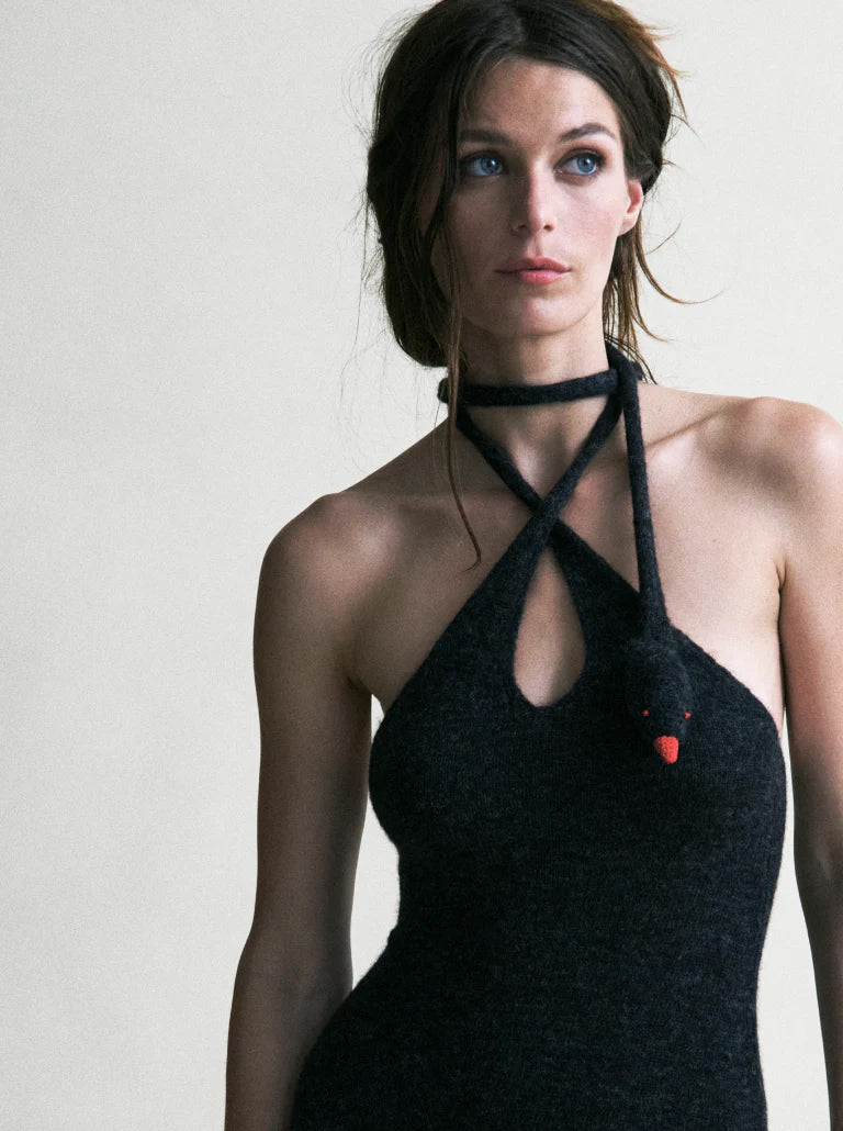 Woman wearing a black halter neck dress with a unique design on a plain background