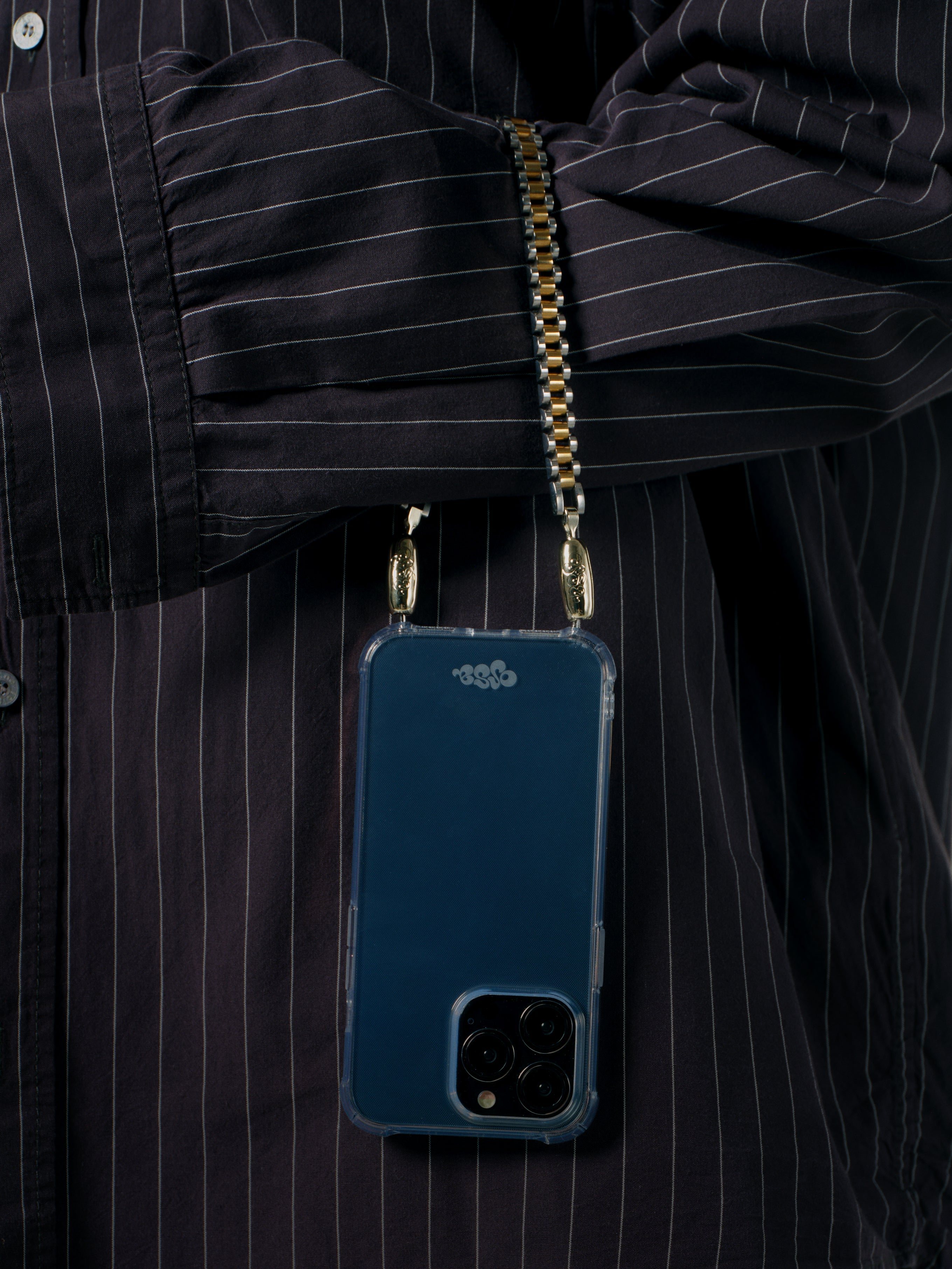 Blue phone case with gold chain held by a person wearing a black pinstripe shirt.
