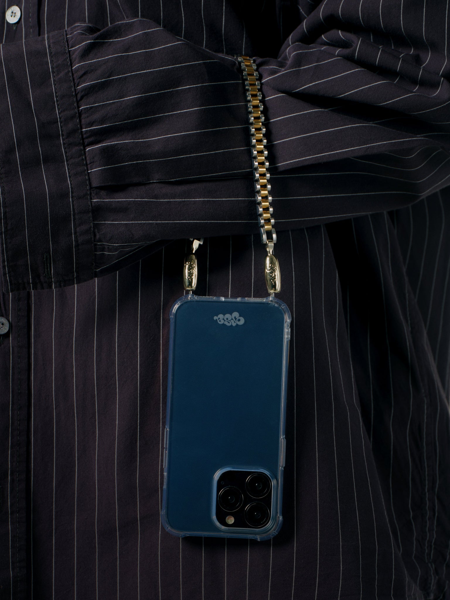 Blue phone case with gold chain held by a person wearing a black pinstripe shirt.