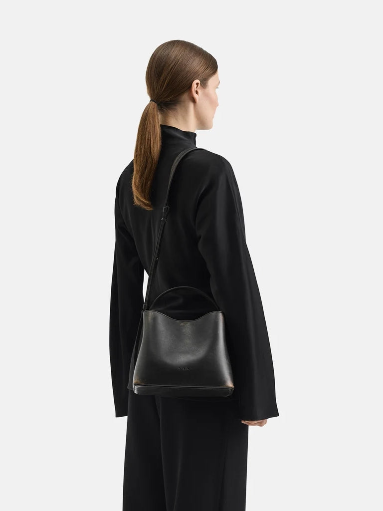 Model carrying Aesther Ekme Mini Sac in vintage black calfskin with a structured silhouette, top handle and adjustable crossbody strap.