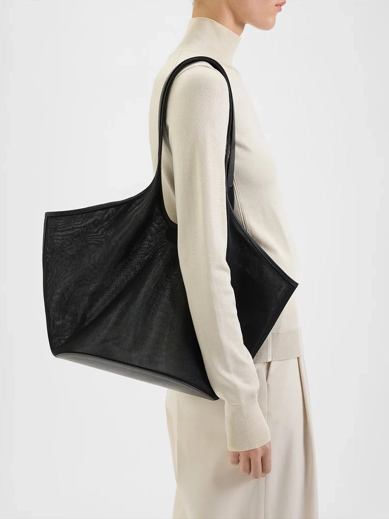 Person wearing a black tote bag over one shoulder on a white background