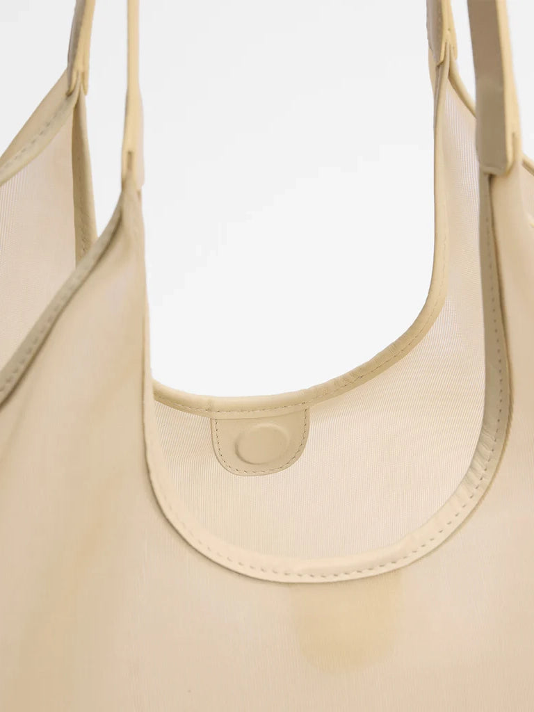 Close-up of a beige handbag with a visible brand logo on a light gray background