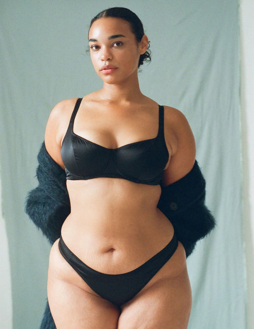 Woman wearing a black bra and underwear set against a light green background