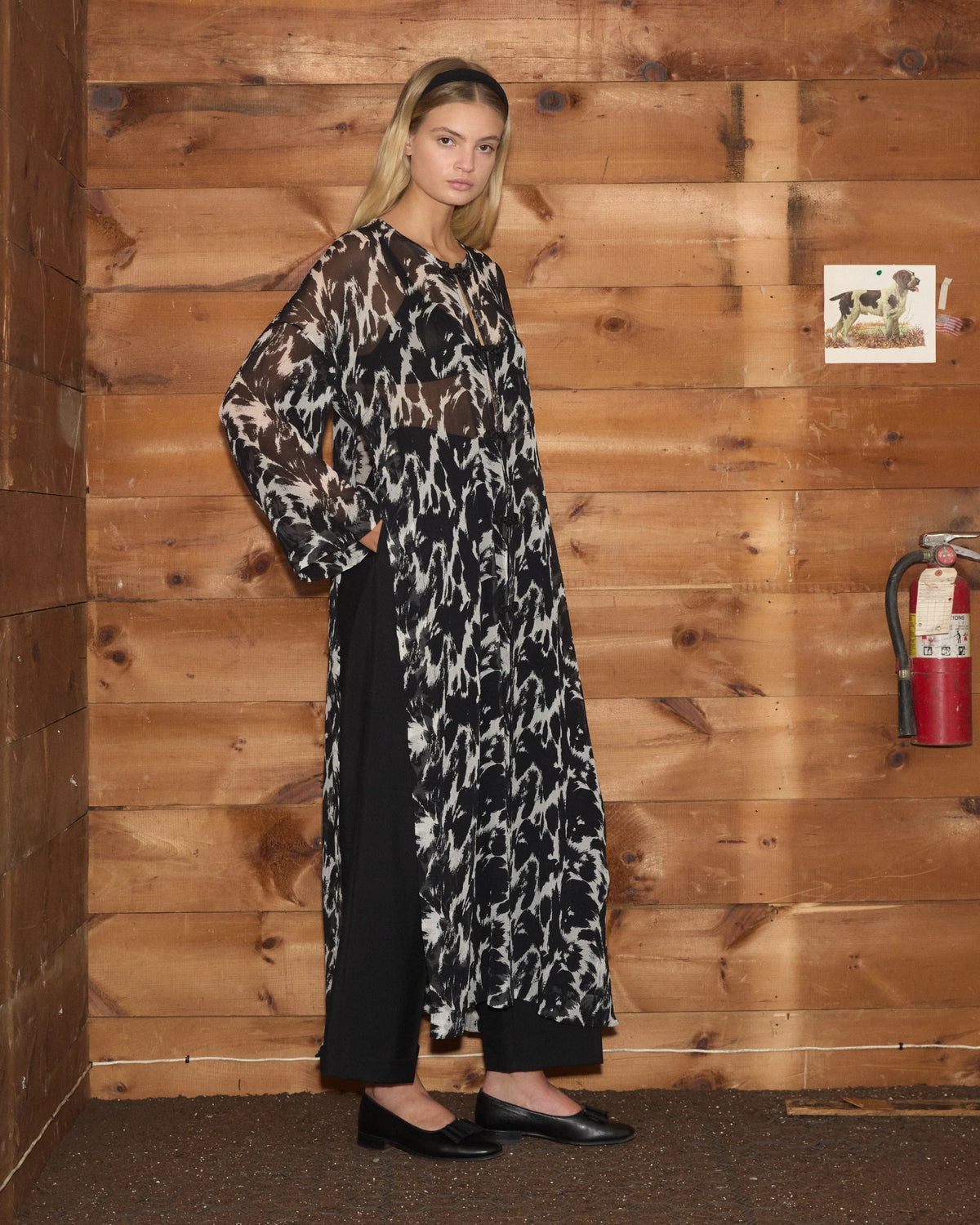 Model wearing Bode Appaloosa Kaftan in black and white textured silk crepe with an all-over spotted print and black frog closures.