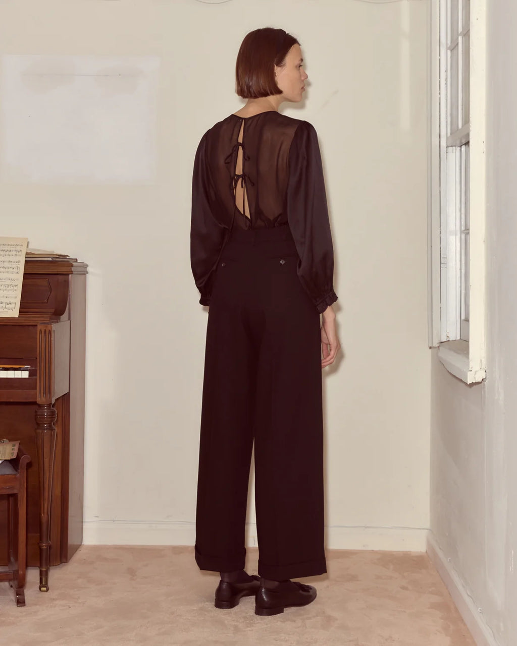Person wearing a black outfit with a sheer back in a room with a piano.