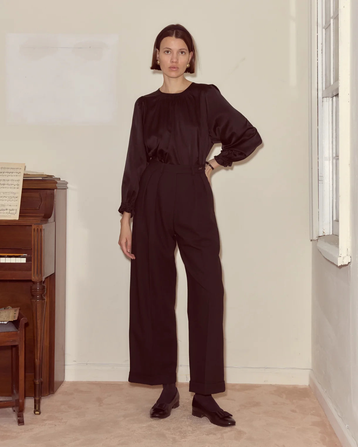 Woman wearing a dark brown jumpsuit standing in a room with a piano.