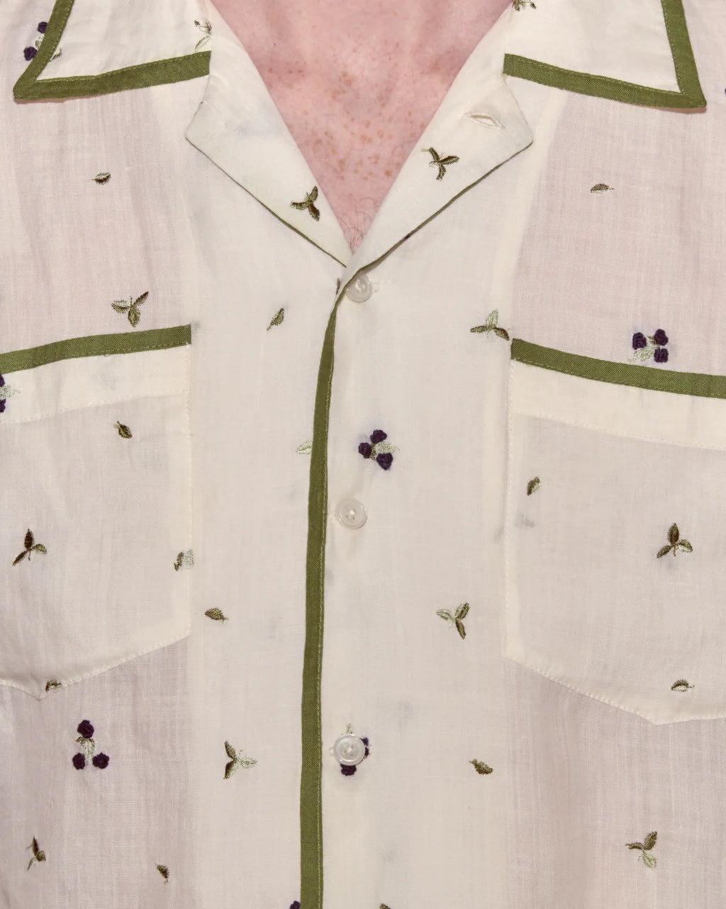 Close-up of a white shirt with green trim and small embroidered details on a pink background