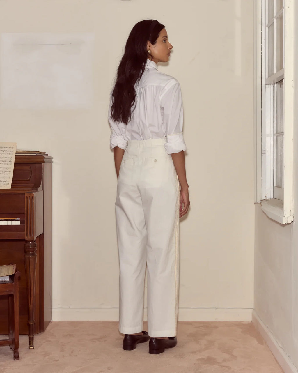 Woman wearing a white shirt and pants standing in a room with a piano.