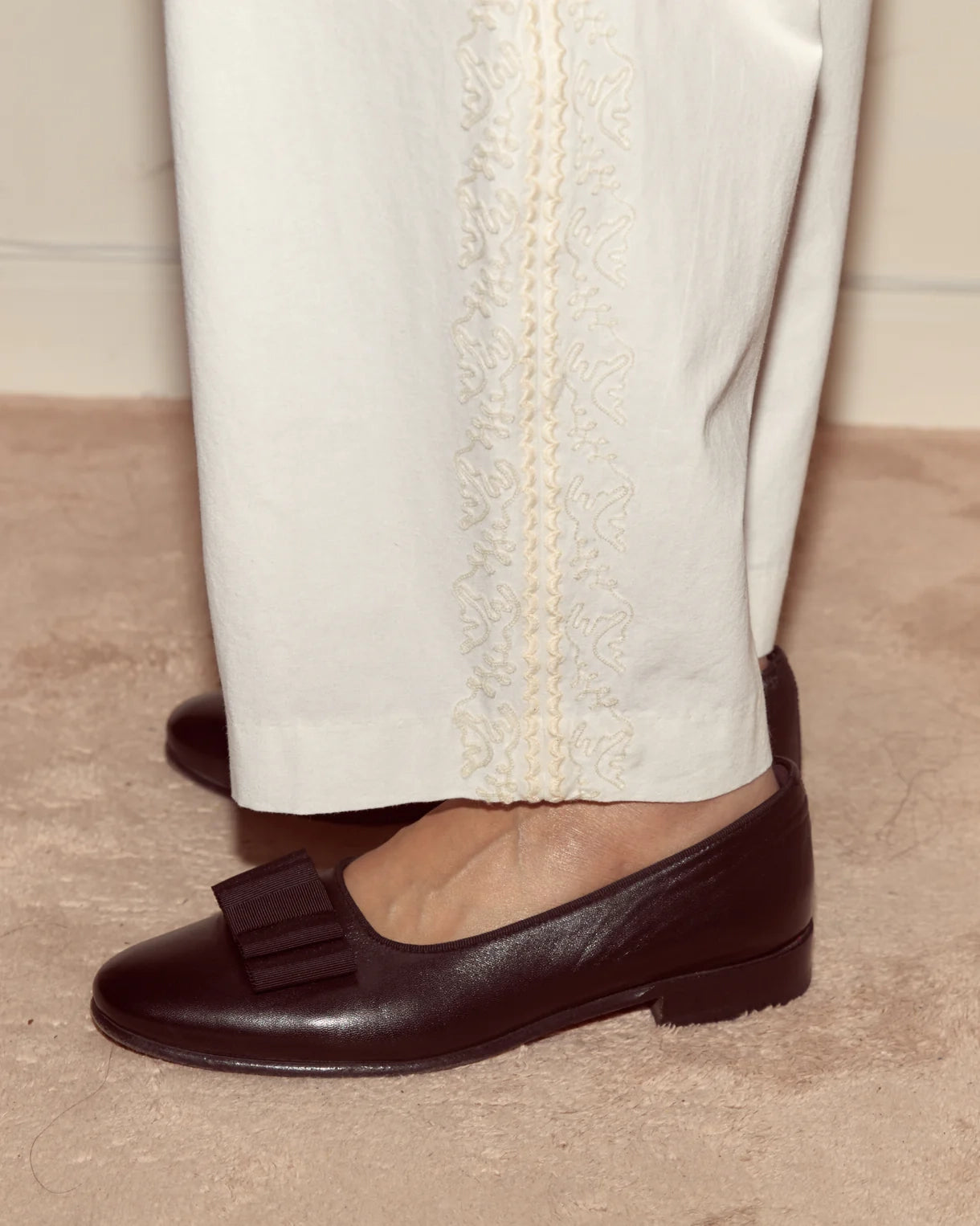 Brown loafers worn with white pants on a neutral background