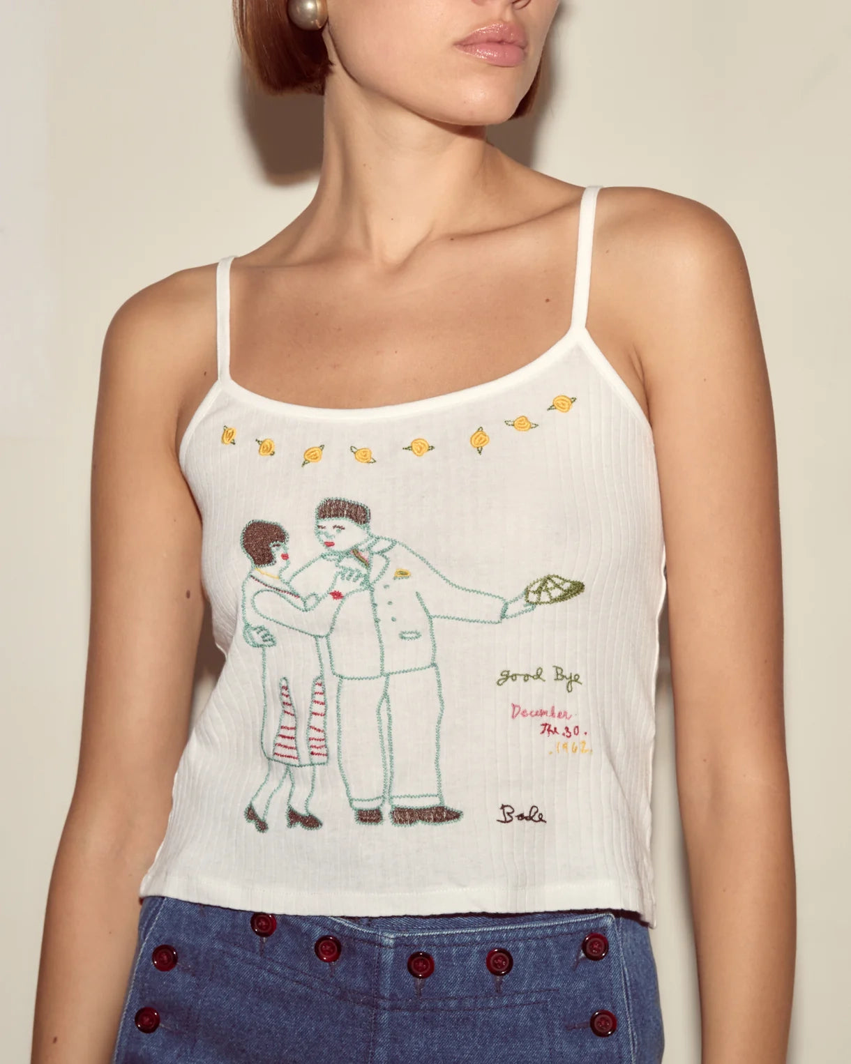 White tank top with embroidered design of a couple and text, worn by a person.
