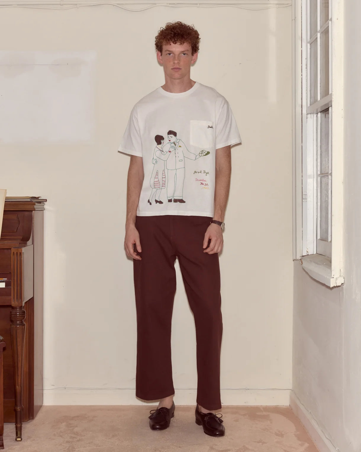 Man wearing a white t-shirt with a graphic design and brown pants in a room.