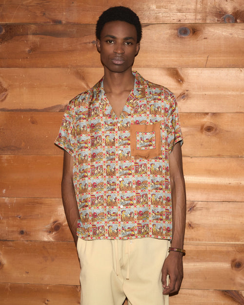 Model wearing Bode Cowboy Comic Short Sleeve Shirt in multicolor silk with a repeating cowboy comic print and front patch pocket.