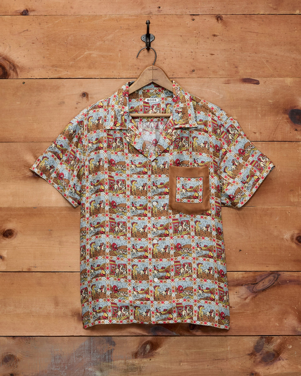 Bode Cowboy Comic Short Sleeve Shirt in multicolor silk with a repeating cowboy comic print and front patch pocket.