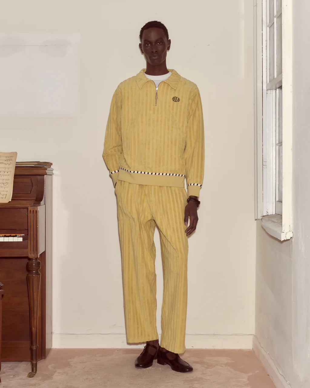 Man wearing a yellow outfit standing in a room with a wooden piano.