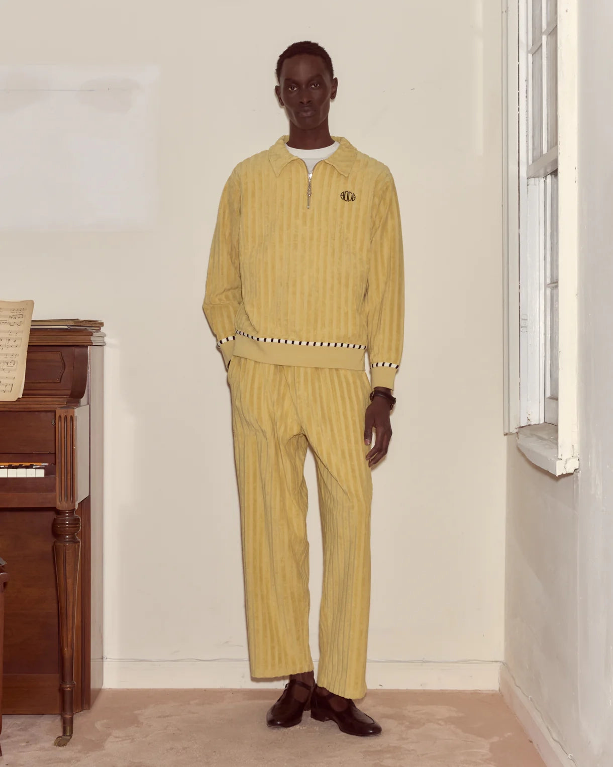 Man wearing a yellow outfit standing in a room with a wooden piano.