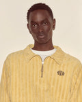 Person wearing a yellow corduroy jacket with a brand logo on a beige background