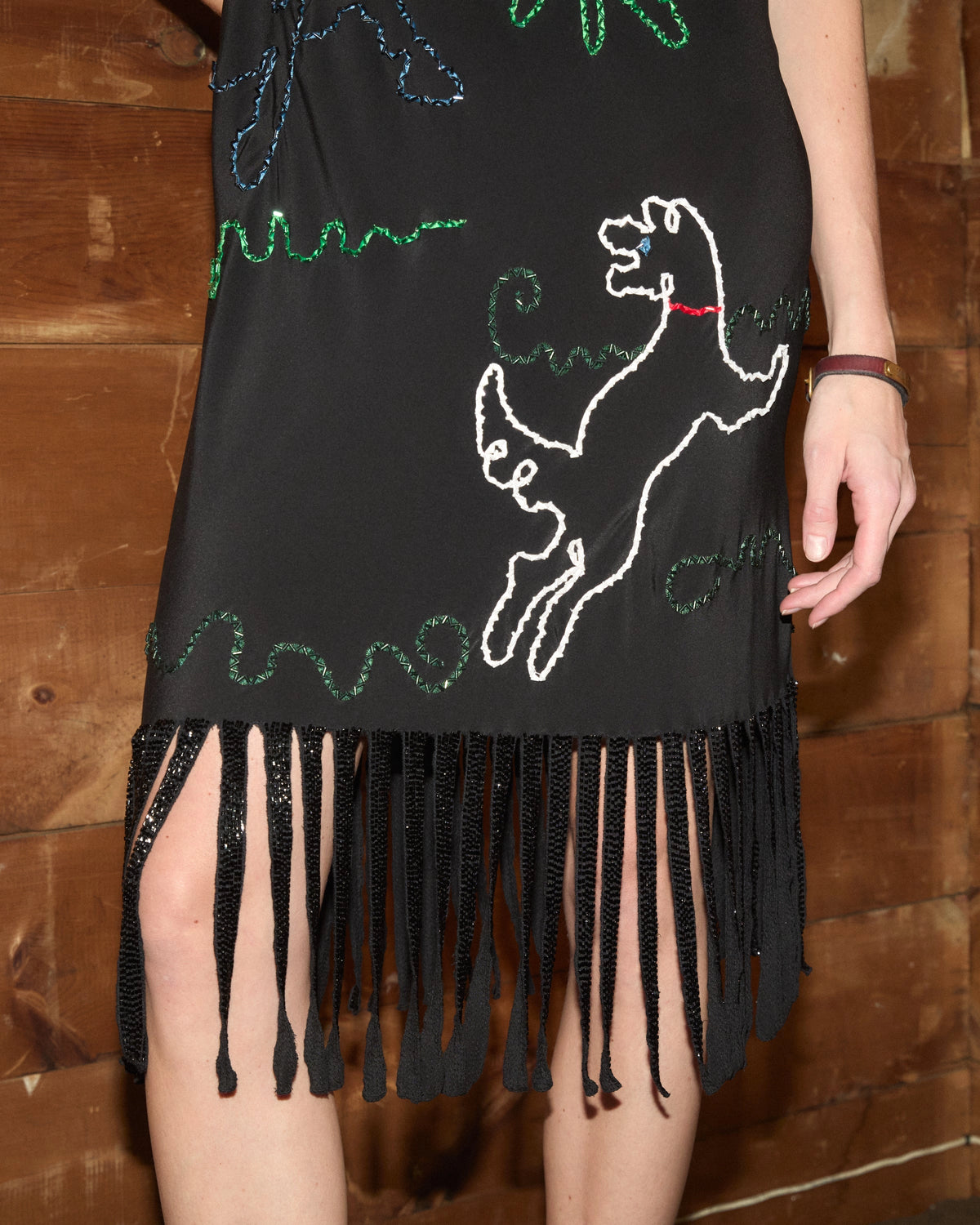 Detail view of Bode Dream Pony Dress in black silk with multicolor beaded doodle motifs, thin shoulder straps and a fringed hem.