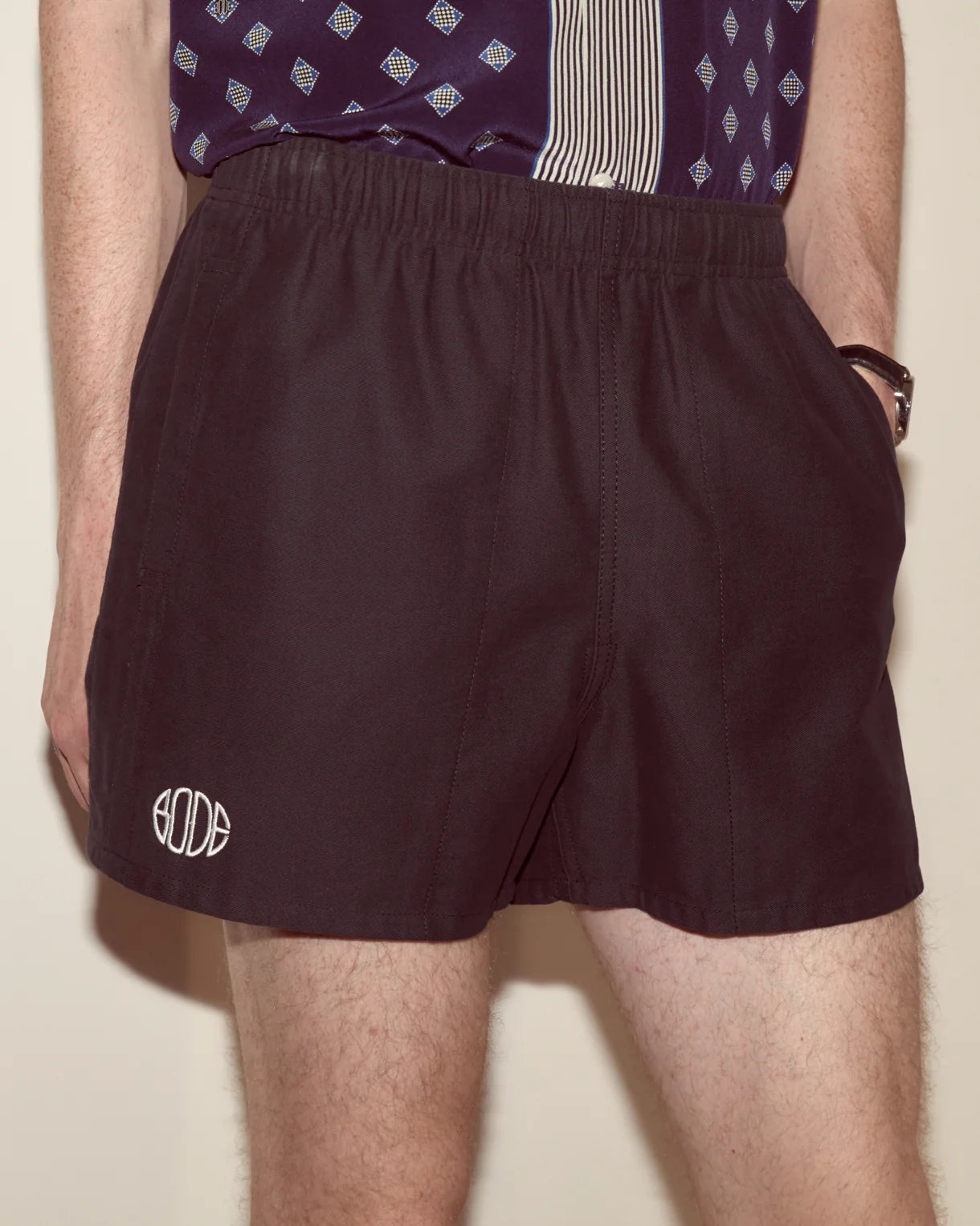 Person wearing maroon shorts with a logo on a beige background