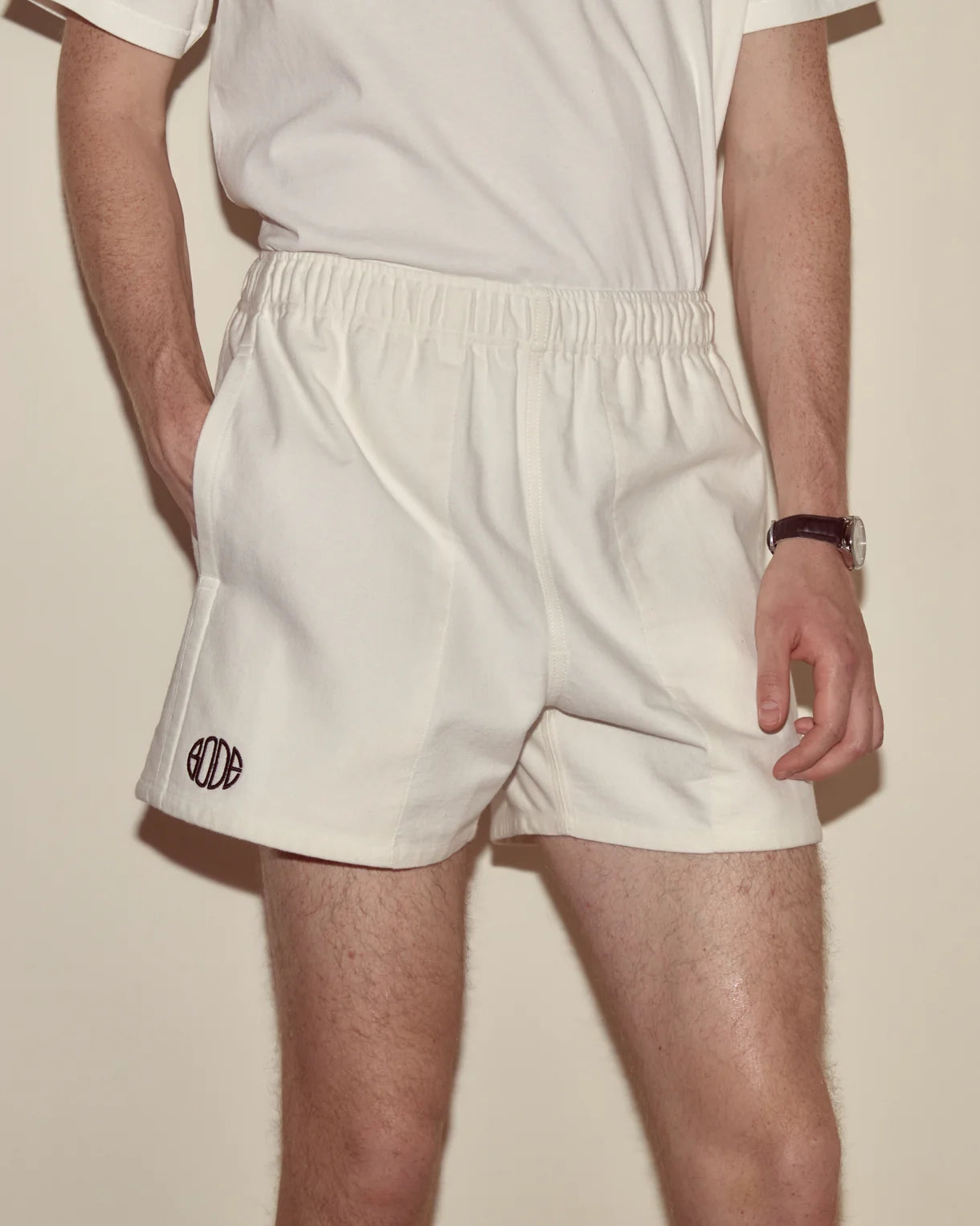 Person wearing white shorts with a logo on a plain background