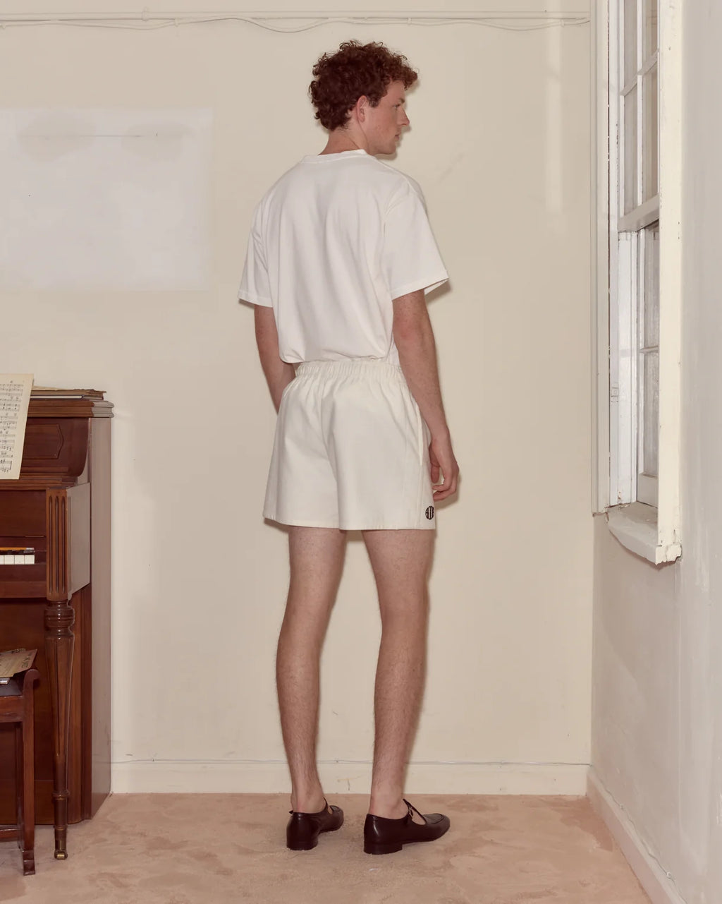 Person wearing a white t-shirt and shorts standing in a room with a piano.