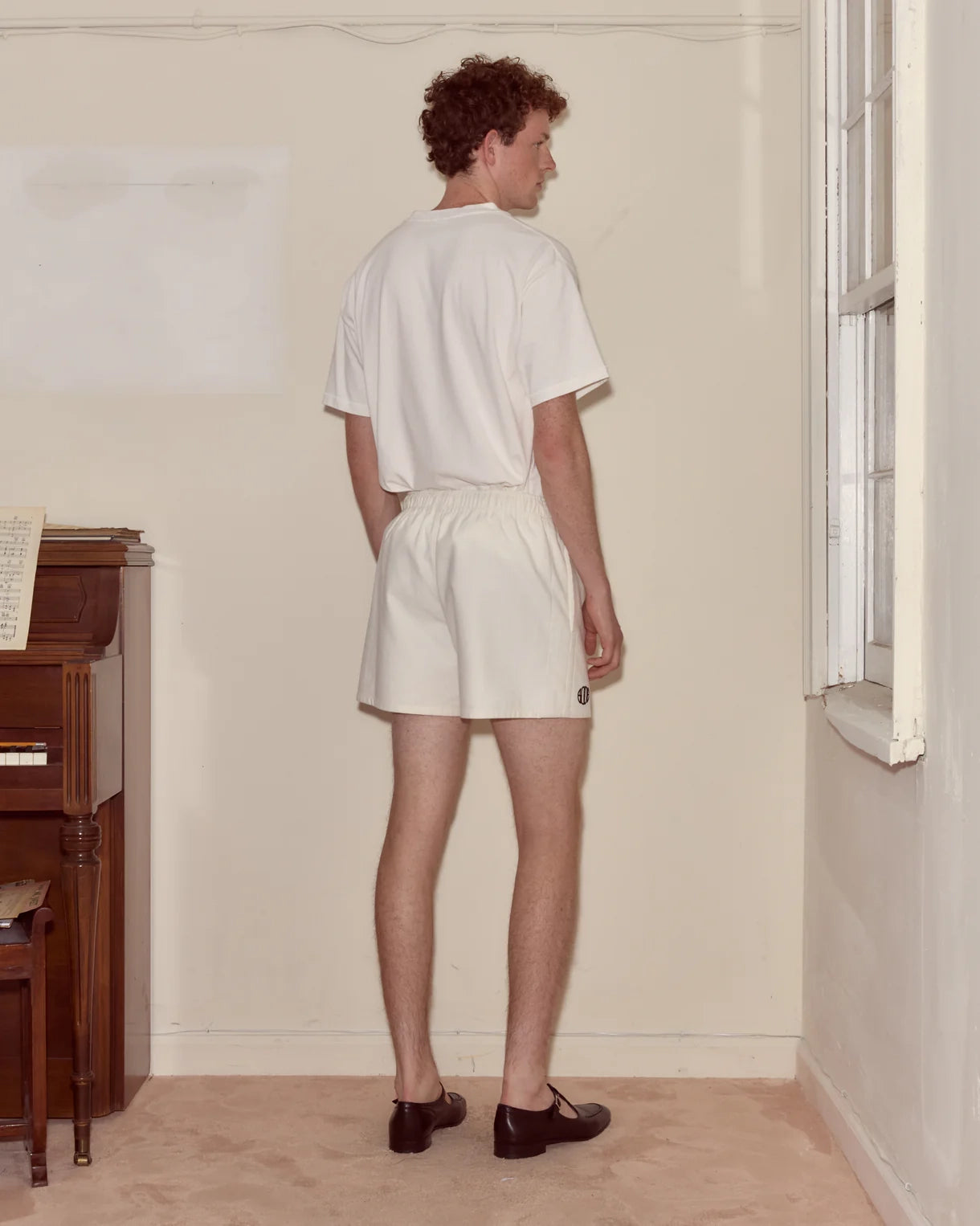 Person wearing a white t-shirt and shorts standing in a room with a piano.