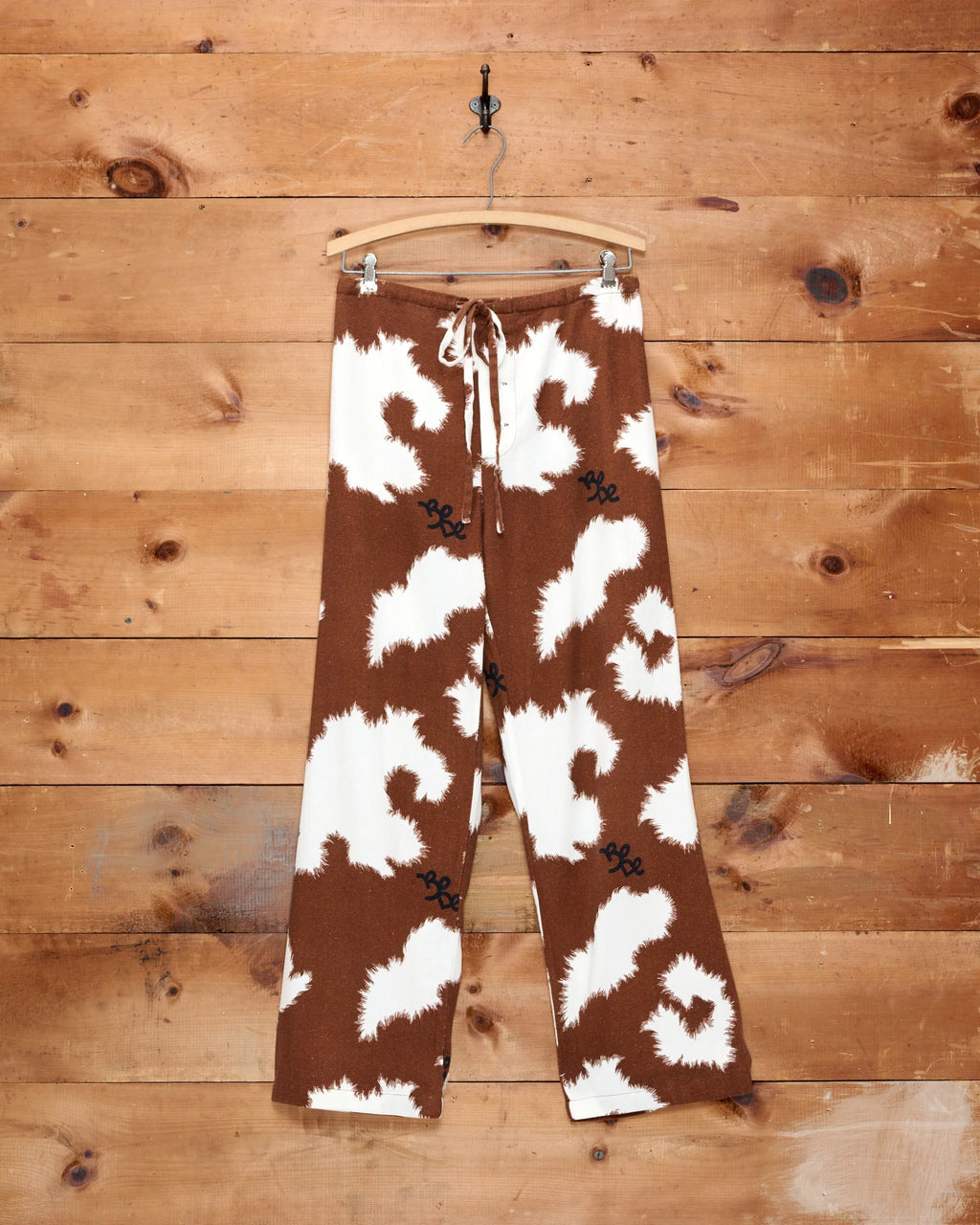 Bode Flannel Cow Print Pajama Pants in brown and white with green piping and cattle brand logo.