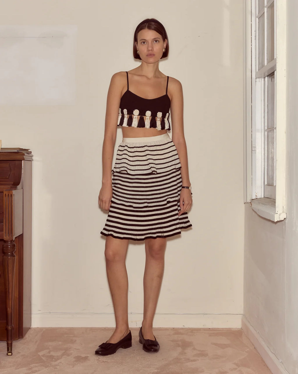 Woman wearing a black and white striped skirt and crop top in a room with a window.