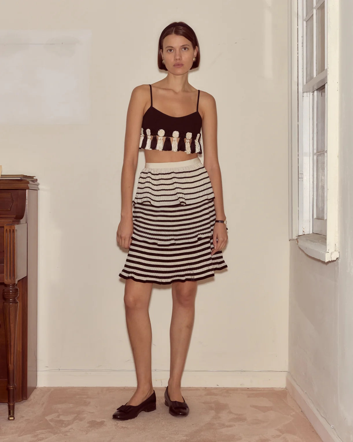 Woman wearing a black and white striped skirt and crop top in a room with a window.