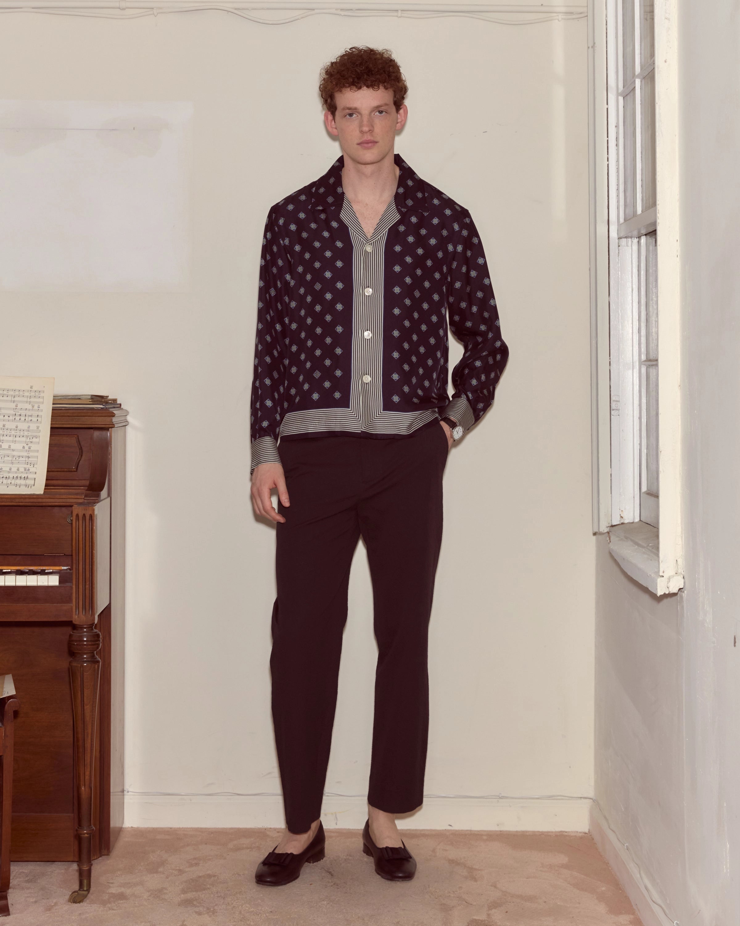 Model wearing navy Bode silk long-sleeve shirt with diamond foulard print and striped trim.